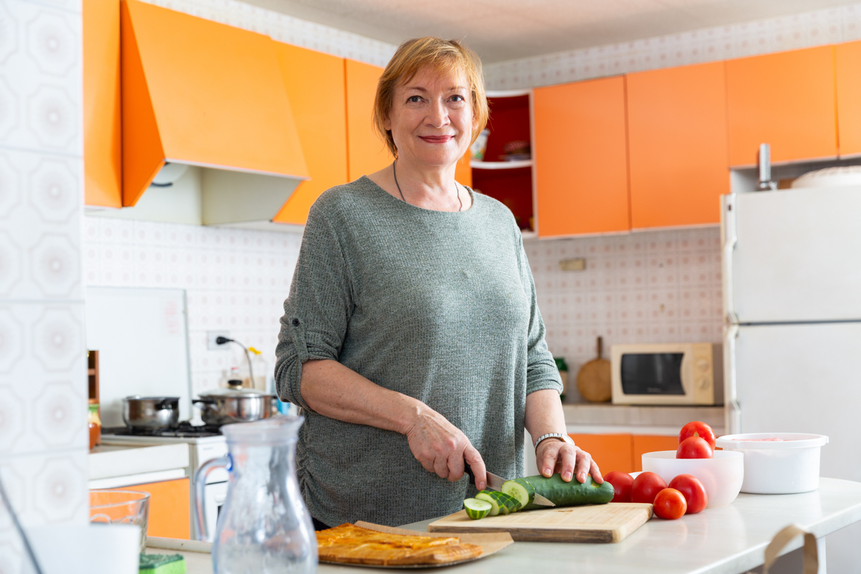 Kuvituskuva, jossa nainen leikkaa kurkkua omassa keittiössään ja hymyilee kameralle
